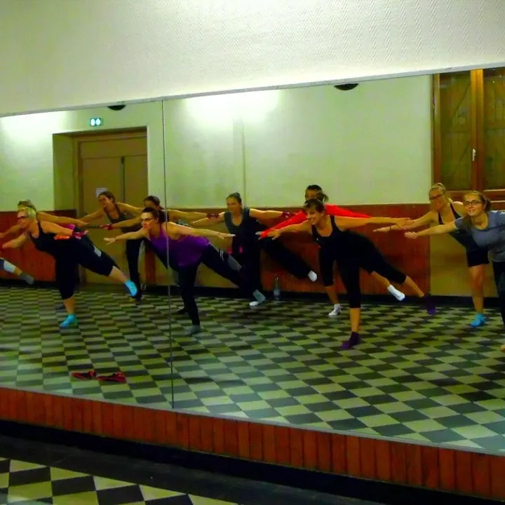Salle à miroirs et carrelage en damier : le groupe en équilibre, bras tendus et jambe en arrière