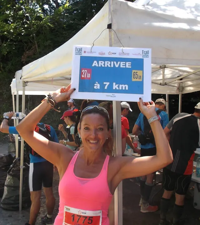 Bras levés sous un panneau « Arrivée à 7 km », dossard à la taille