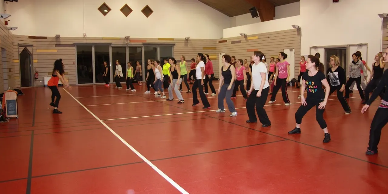 Salle de sport au sol rouge remplie de participantes en plein mouvement