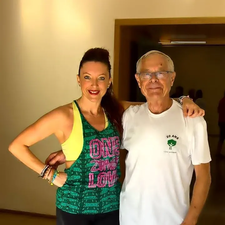 Une femme en débardeur « One Zumba Love » bras dessus bras dessous avec un participant aux cheveux blancs