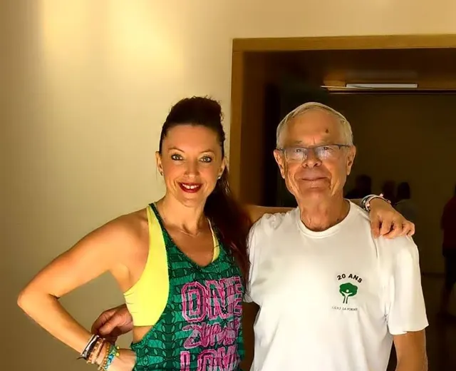 Une femme en débardeur « One Zumba Love » bras dessus bras dessous avec un participant aux cheveux blancs